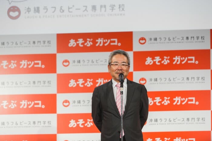 Nobuhiko Horie sube al escenario en la conferencia de prensa para anunciar el esquema de "Okinawa Rough & Peace College"